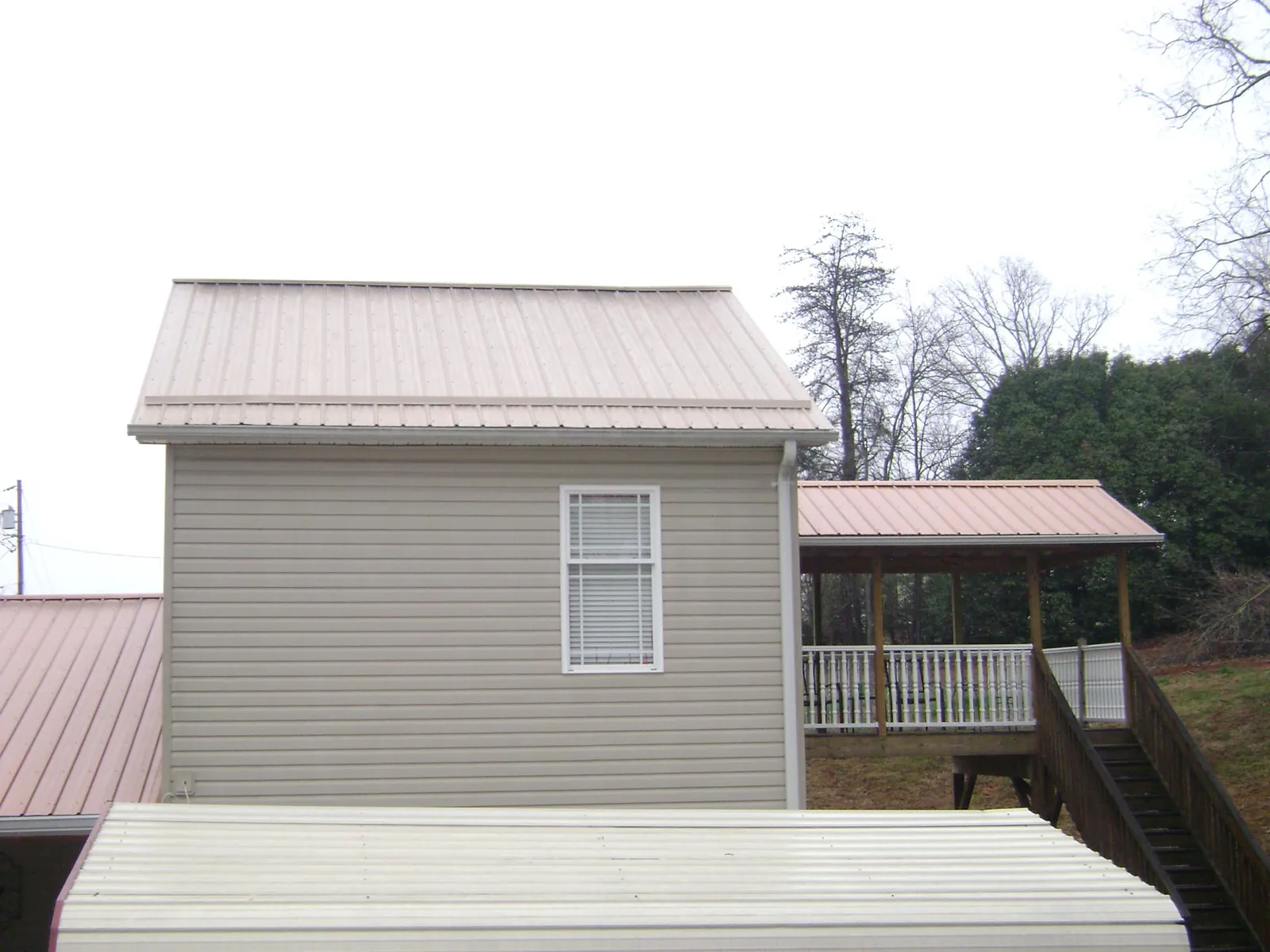 Tan metal roofs on a two story addition and attached porch, from a Roof Replacement job in Hope